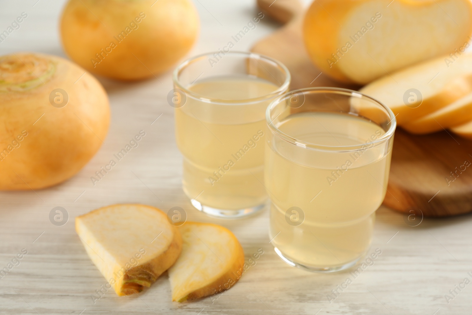 Photo of Glasses of fresh natural turnip juice, cut and whole roots on white wooden table