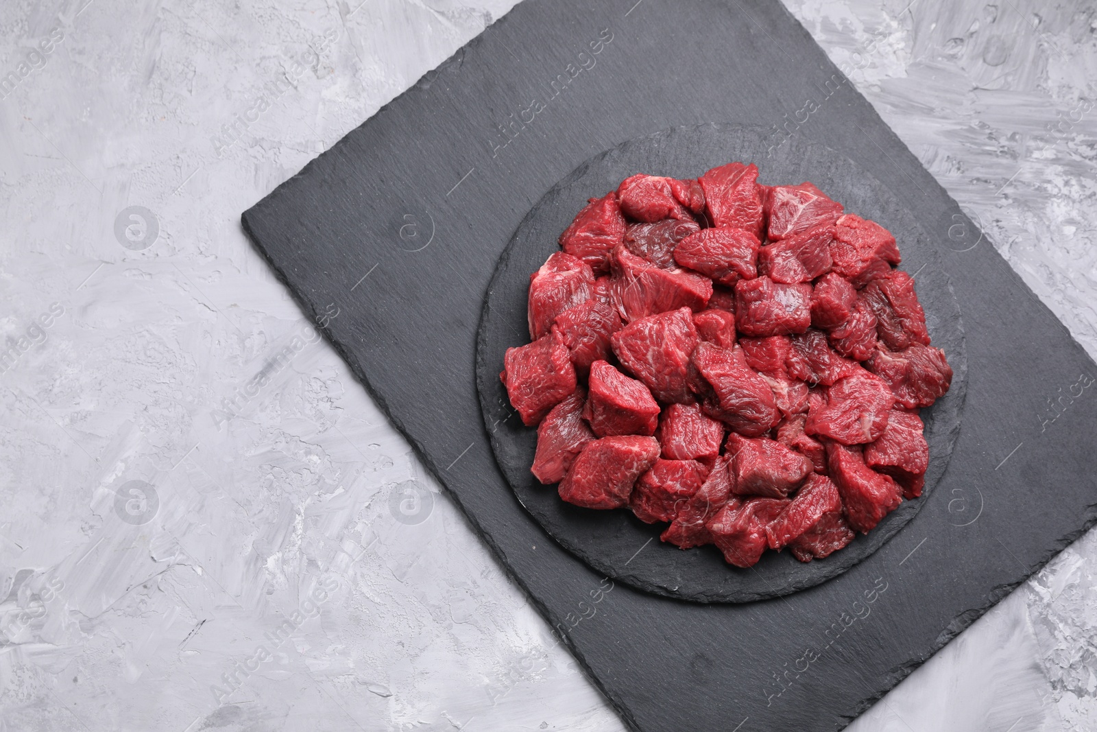 Photo of Pieces of raw beef meat on grey textured table, top view. Space for text
