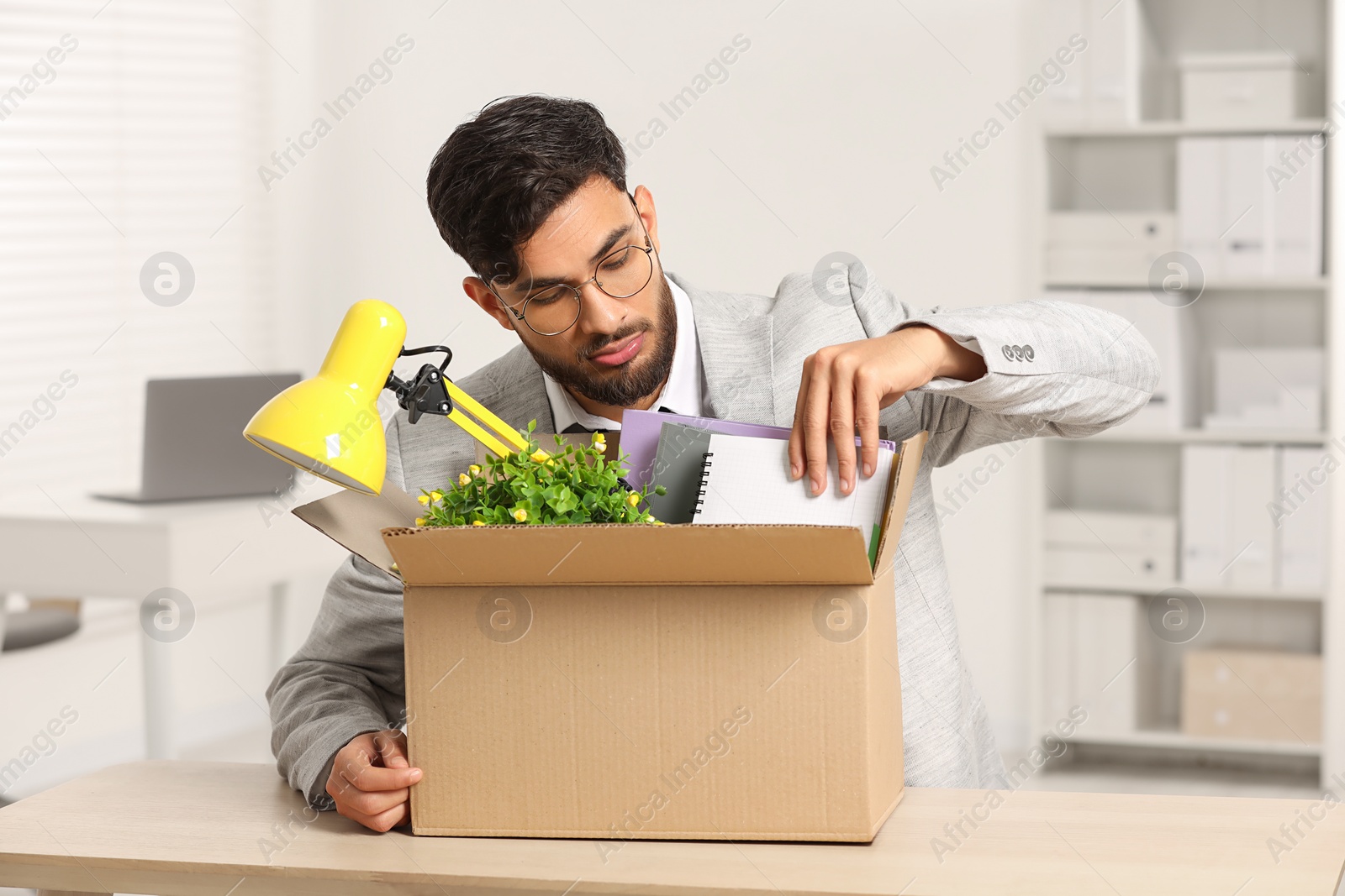 Photo of Unemployment problem. Frustrated man with box of personal belongings at desk in office