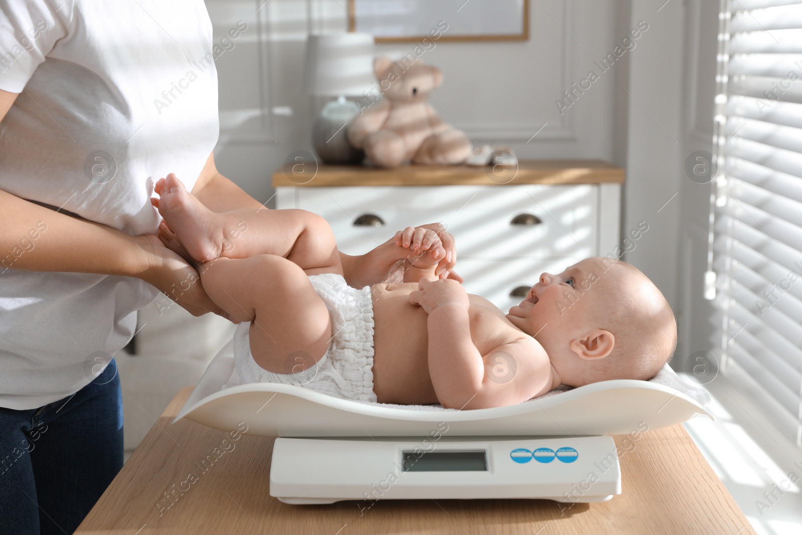 Photo of Young woman weighting her cute baby at home, closeup. Health care