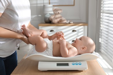 Photo of Young woman weighting her cute baby at home, closeup. Health care