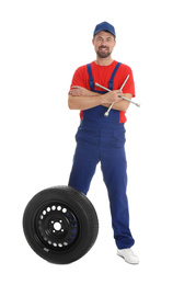 Full length portrait of professional auto mechanic with lug wrench and wheel on white background