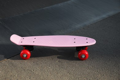 Photo of Modern pink skateboard with red wheels on asphalt road outdoors
