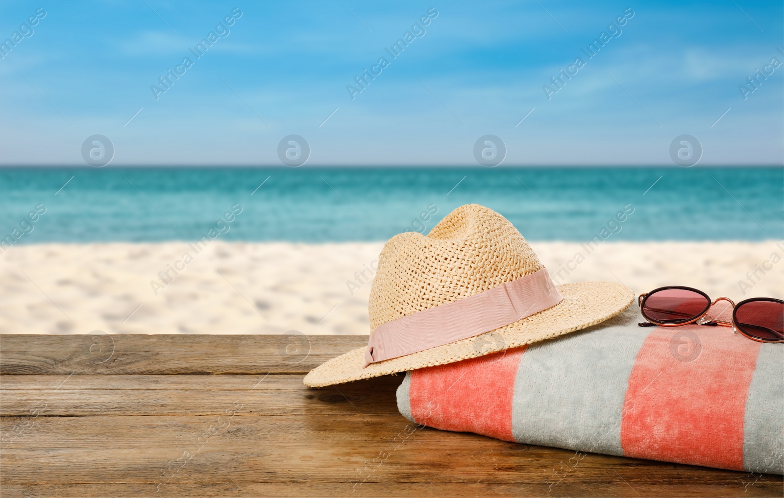 Image of Beach towel, straw hat and sunglasses on wooden surface near seashore. Space for text 