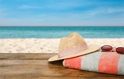 Image of Beach towel, straw hat and sunglasses on wooden surface near seashore. Space for text 