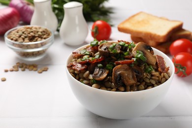 Delicious lentils with mushrooms, bacon and green onion in bowl served on white table, closeup