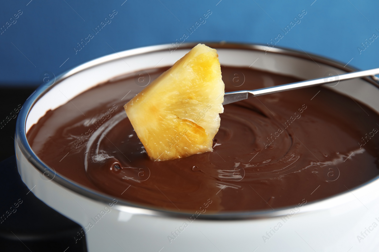 Photo of Dipping pineapple into pot with tasty chocolate fondue, closeup