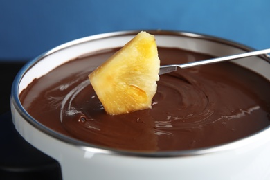 Photo of Dipping pineapple into pot with tasty chocolate fondue, closeup