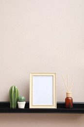 Empty photo frame, cactus figures and air reed freshener on shelf near pink wall, space for text
