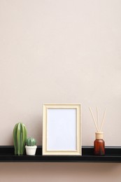 Photo of Empty photo frame, cactus figures and air reed freshener on shelf near pink wall, space for text