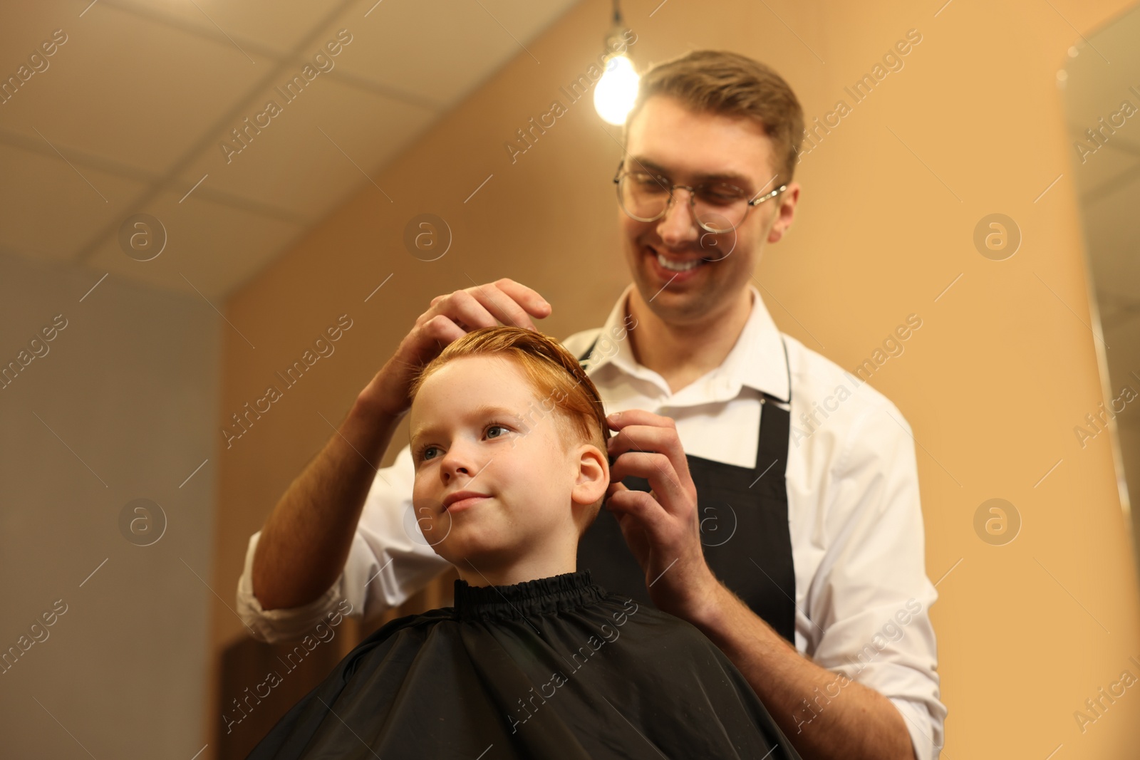 Photo of Professional hairdresser working with boy in beauty salon, low angle view