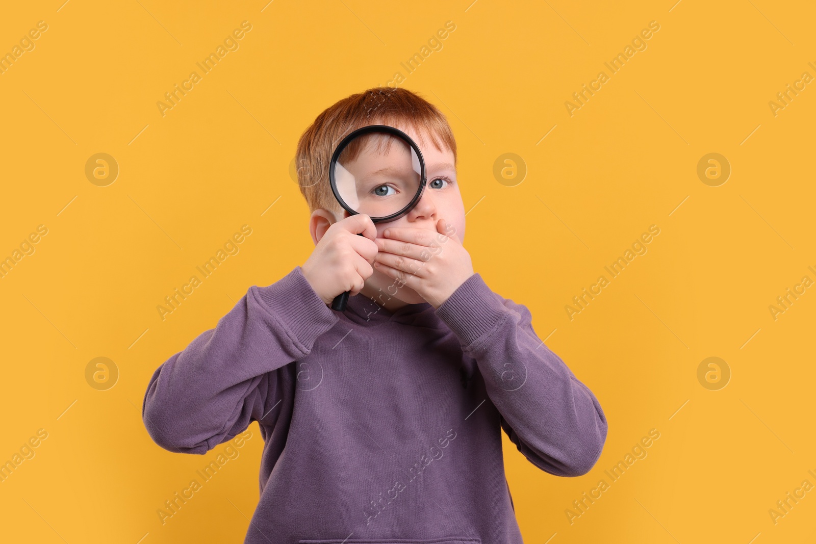 Photo of Surprised boy looking through magnifier glass on yellow background