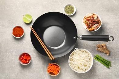 Flat lay composition with black wok surrounded by spices and products on grey textured table