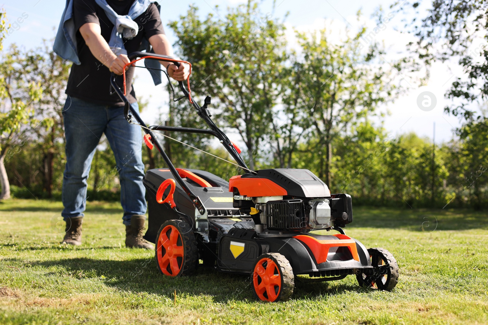 Photo of Man cutting green grass with lawn mower in garden, closeup