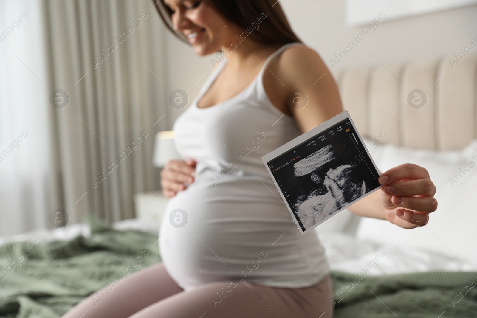 Photo of Young pregnant woman with ultrasound picture of baby in bedroom, closeup