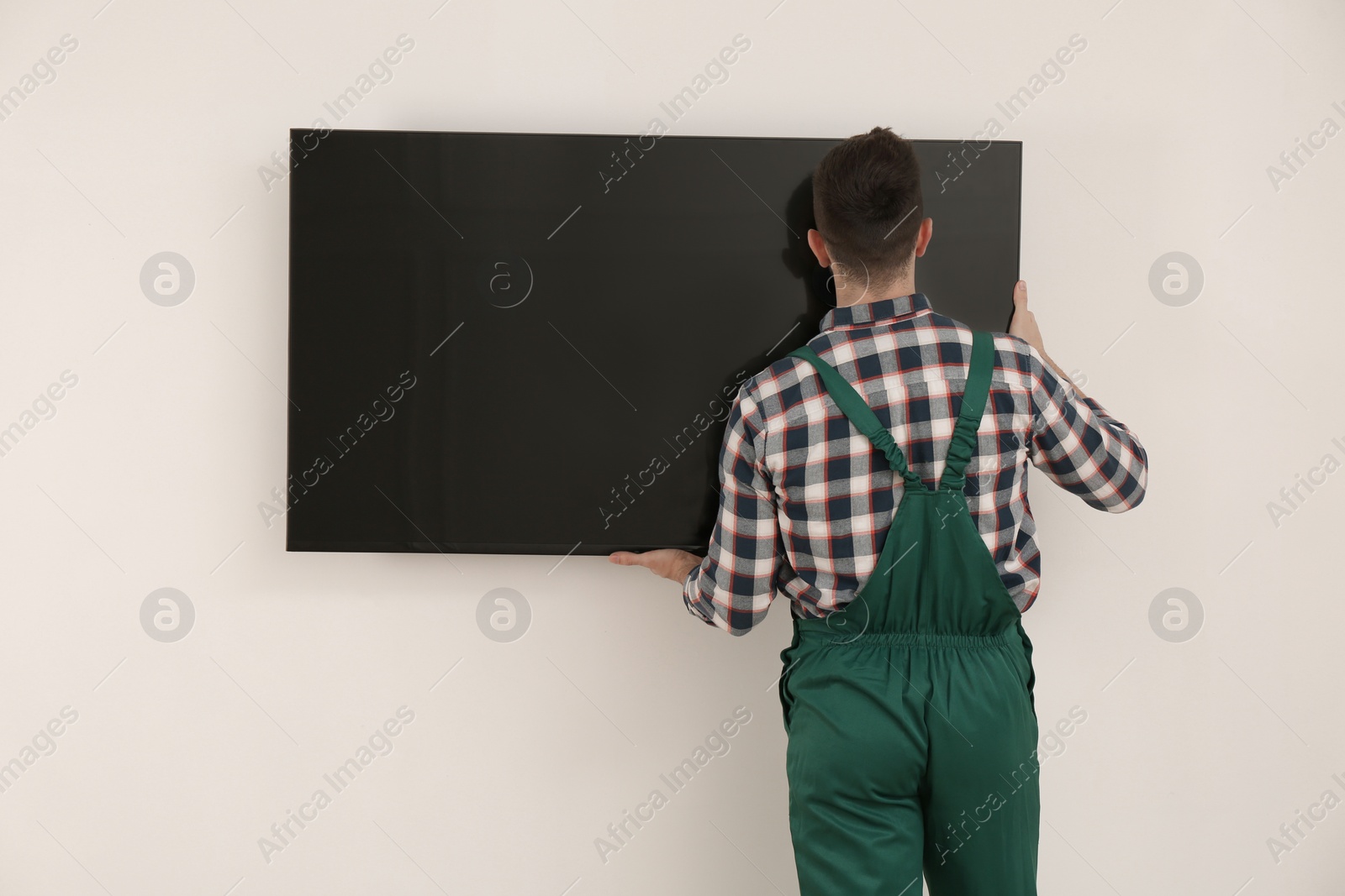 Photo of Professional technician installing modern flat screen TV on wall indoors, back view