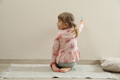Little girl drawing on beige wall indoors, back view. Child`s art