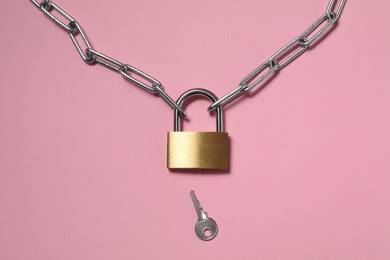 Steel padlock with chain and key on pink background, top view