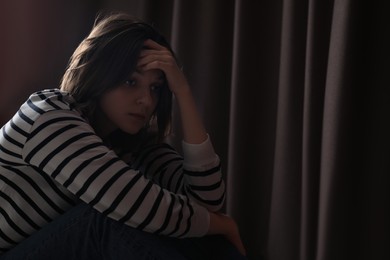 Photo of Sad young woman near curtains indoors, space for text