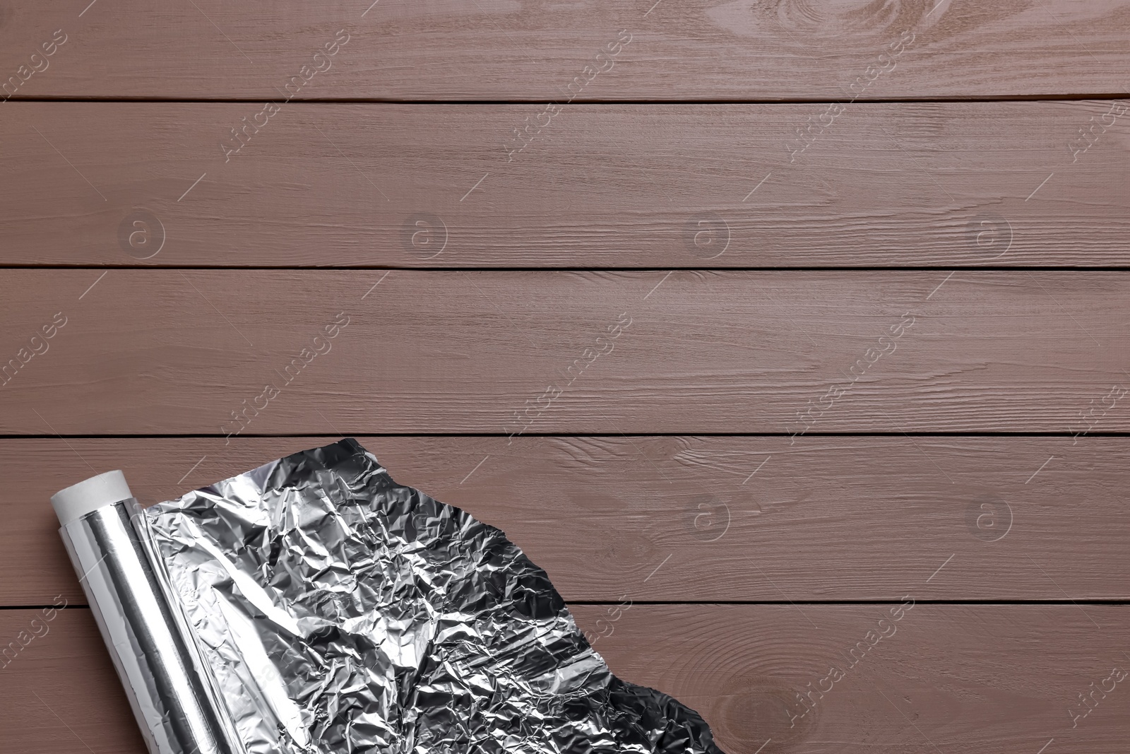 Photo of Roll of aluminum foil on wooden table, top view. Space for text