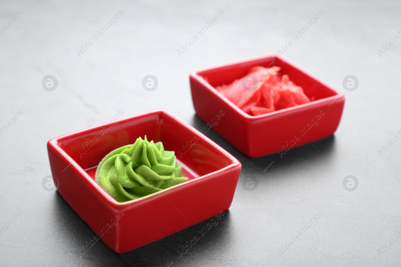 Photo of Bowls with swirl of wasabi paste and pickled ginger on grey table, closeup