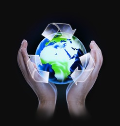 Image of Man holding virtual image of Earth with recycling symbol on dark background, closeup view