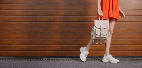 Young woman with stylish backpack near wooden wall, closeup