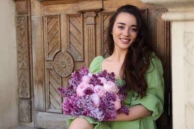 Photo of Beautiful woman with bouquet of spring flowers near wooden door outdoors, space for text