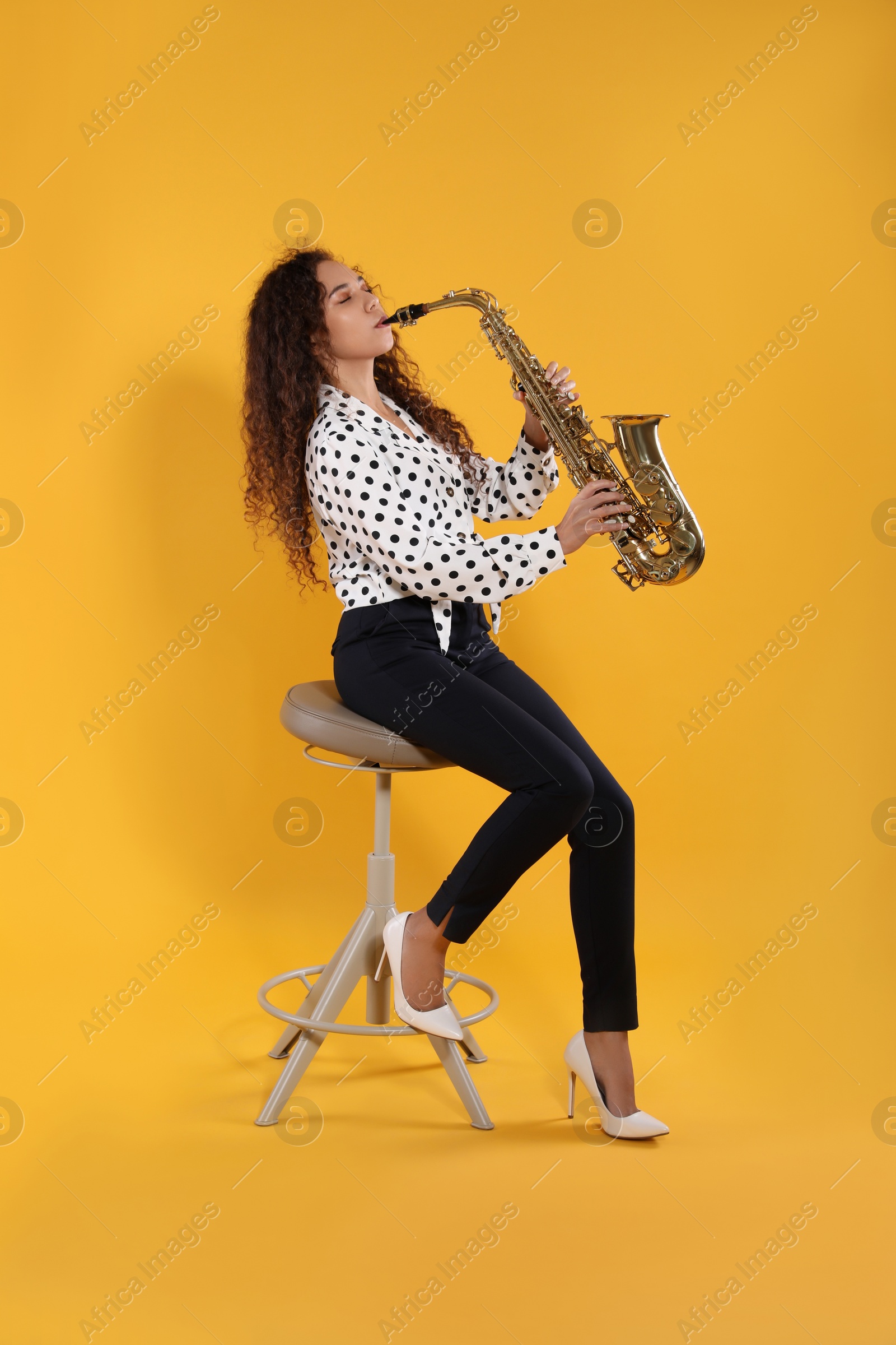 Photo of Beautiful African American woman playing saxophone on yellow background