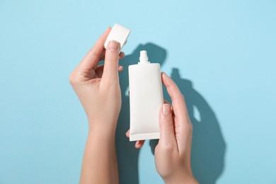 Woman with tube of hand cream on light blue background, top view