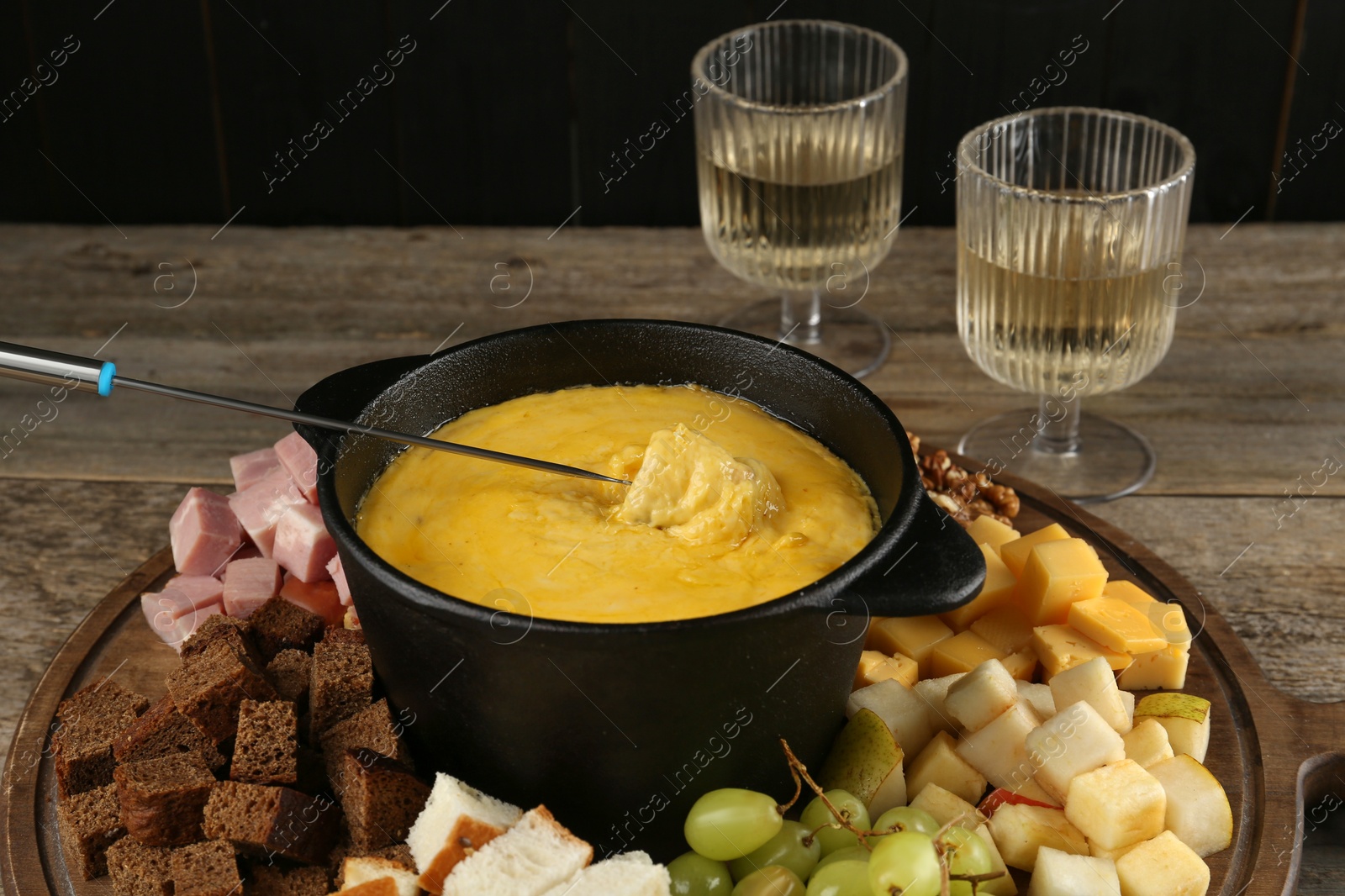 Photo of Fondue pot with melted cheese, glasses of wine and different products on wooden table