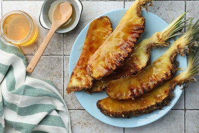 Tasty grilled pineapples, honey and wooden spoon on light gray tiled table, flat lay