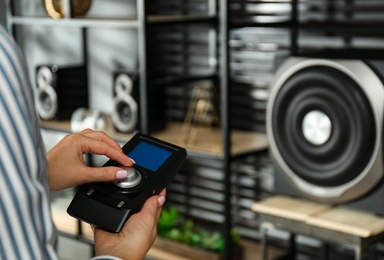 Photo of Woman using remote to control audio speaker system indoors, closeup