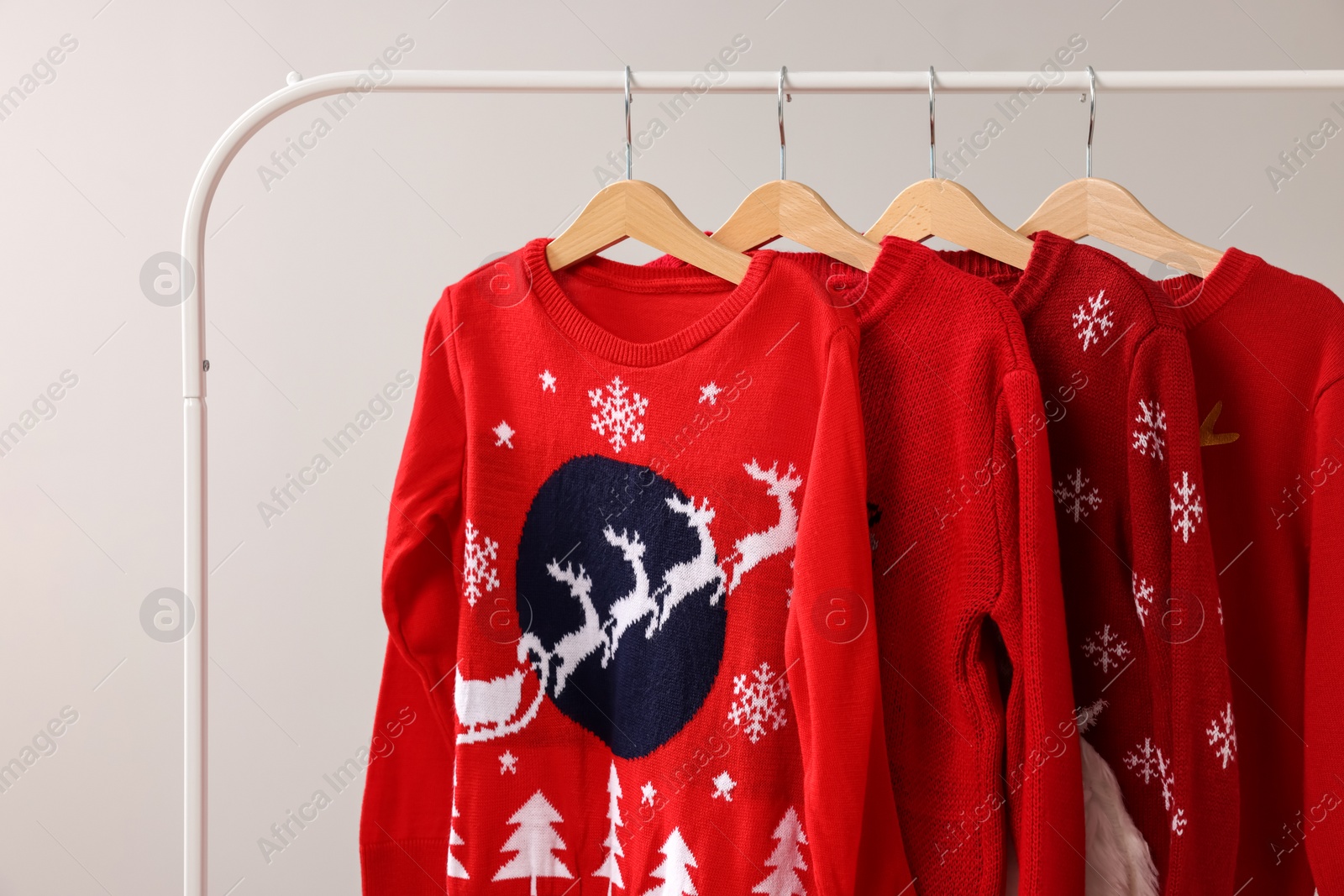 Photo of Different Christmas sweaters hanging on rack against light background