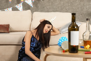 Photo of Young woman sleeping near sofa in messy room after party