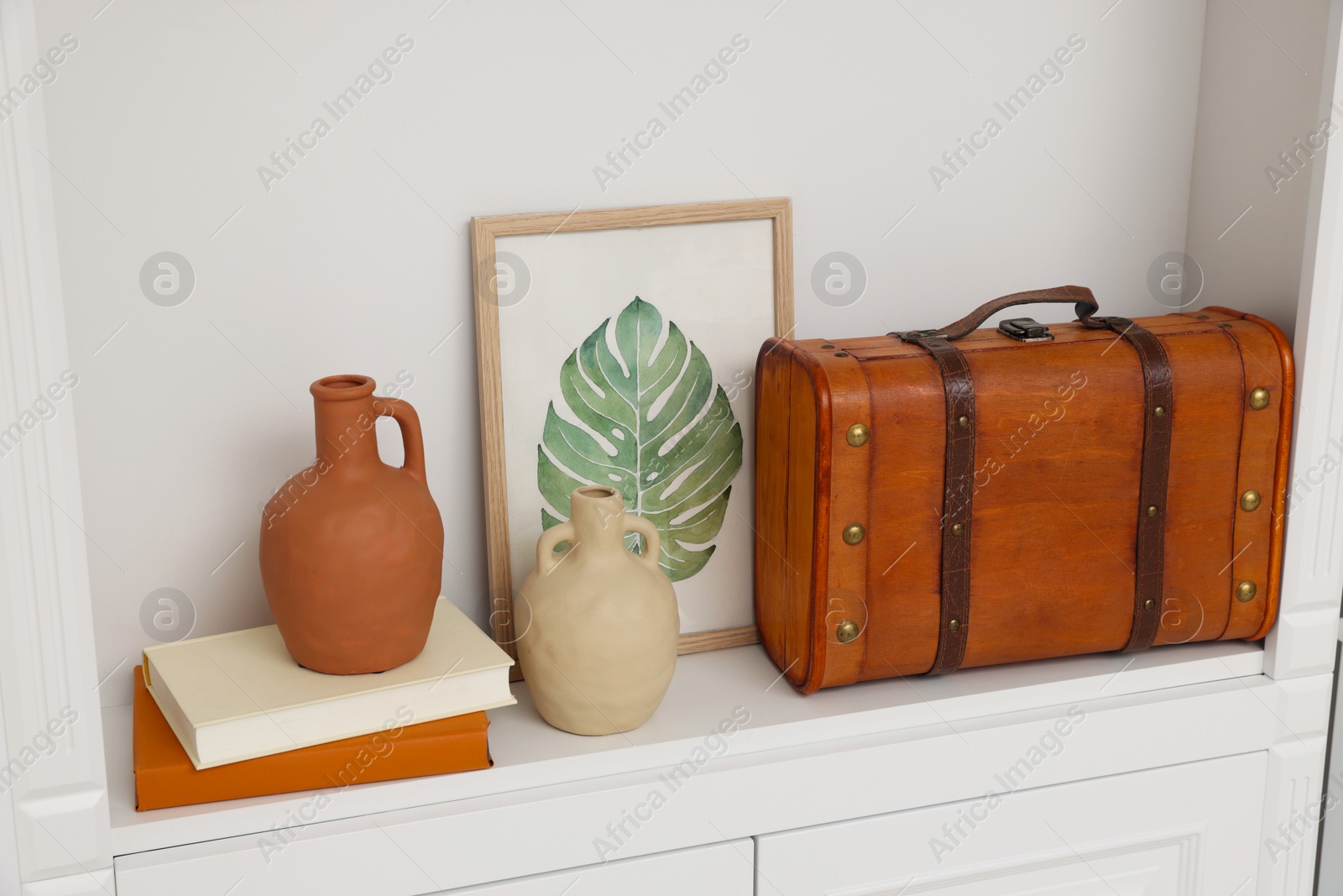 Photo of Brown suitcase, vases, books and picture on shelving unit indoors