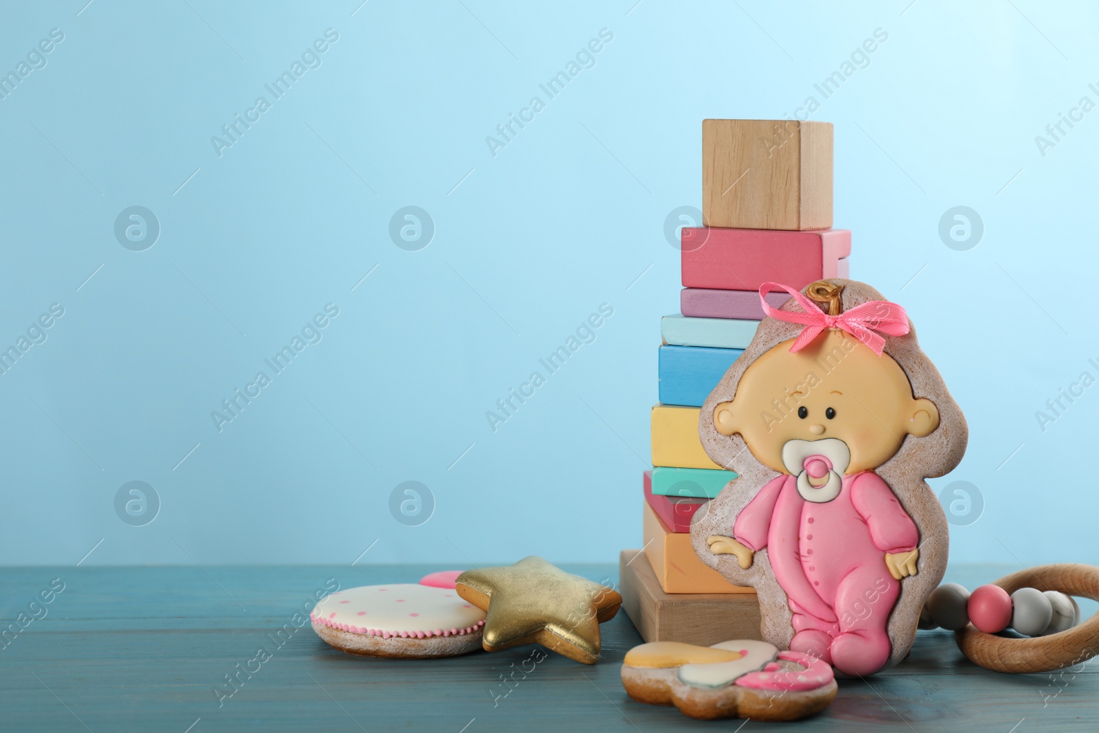 Photo of Tasty cookie in shape of cute baby and toys on light blue wooden table. Space for text