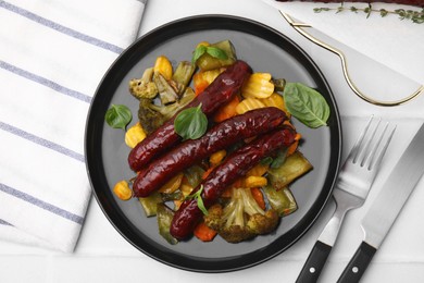 Photo of Delicious smoked sausages and baked vegetables served on white table, flat lay