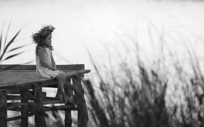 Image of Cute little girl wearing wreath made of beautiful flowers on pier near river, toned in black and white