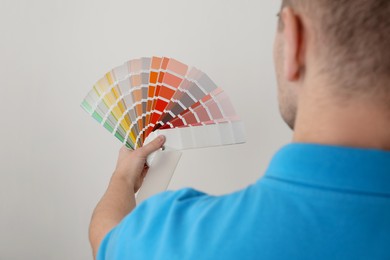 Photo of Man with palette choosing color for painting wall indoors, closeup. Interior design