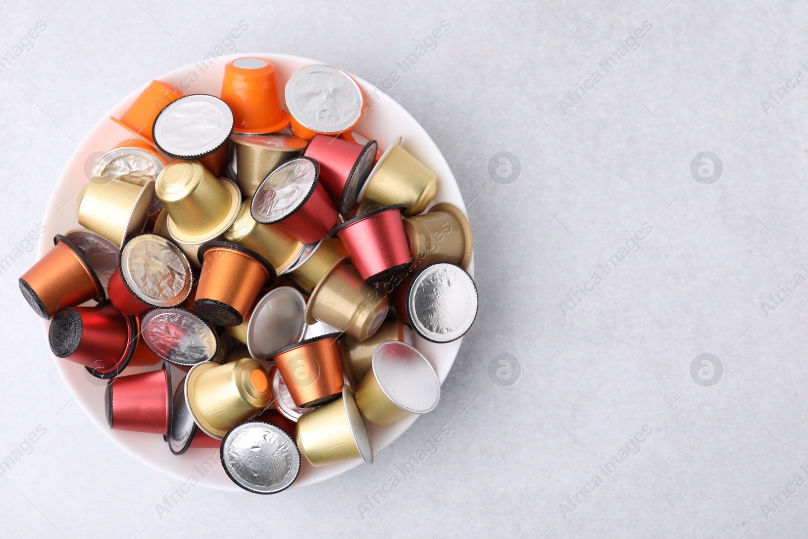 Photo of Bowl of many coffee capsules on light grey table, top view. Space for text