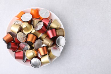 Bowl of many coffee capsules on light grey table, top view. Space for text