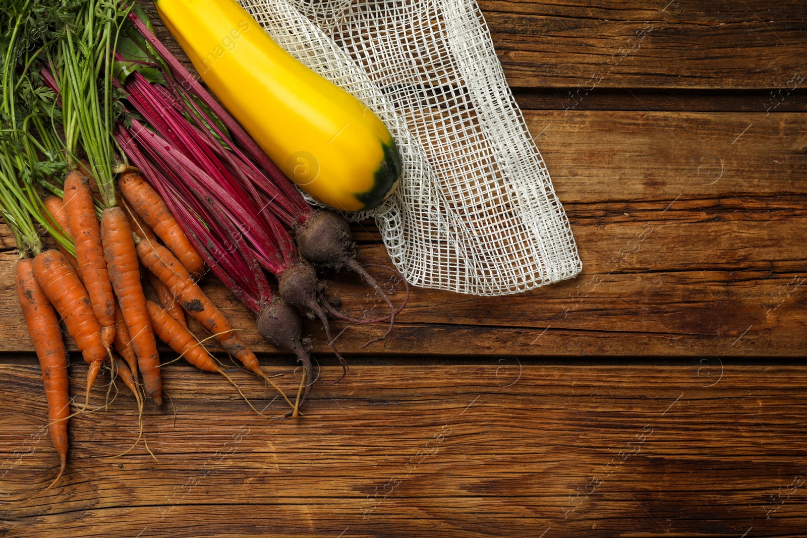 Photo of Carrots, beets, squash and net bag on wooden table, flat lay. Space for text