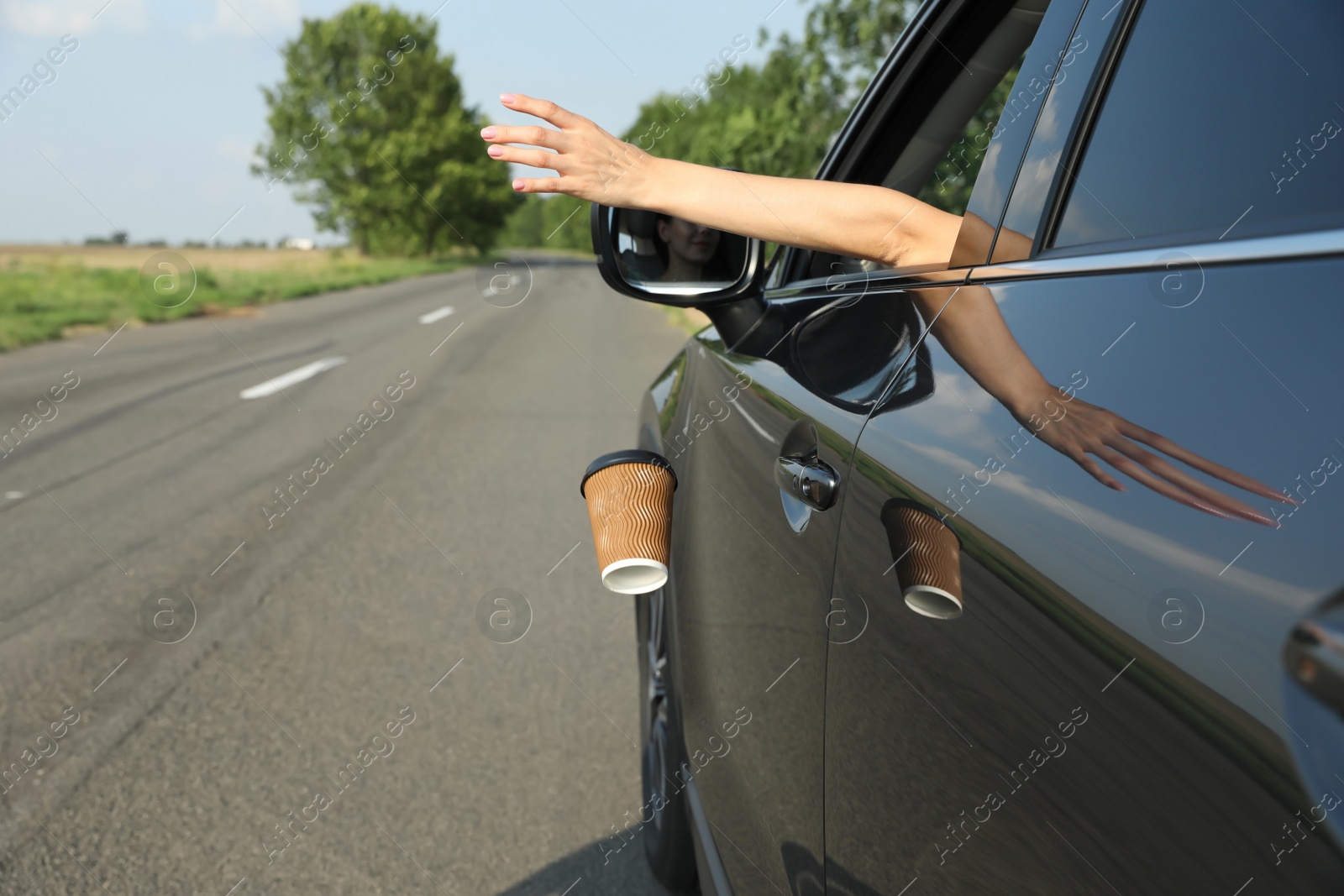 Photo of Driver throwing away paper cup from car window. Garbage on road