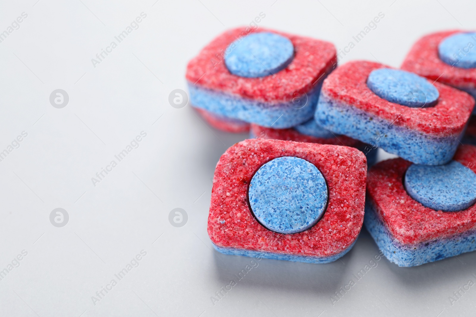 Photo of Many dishwasher detergent tablets on light background, closeup. Space for text