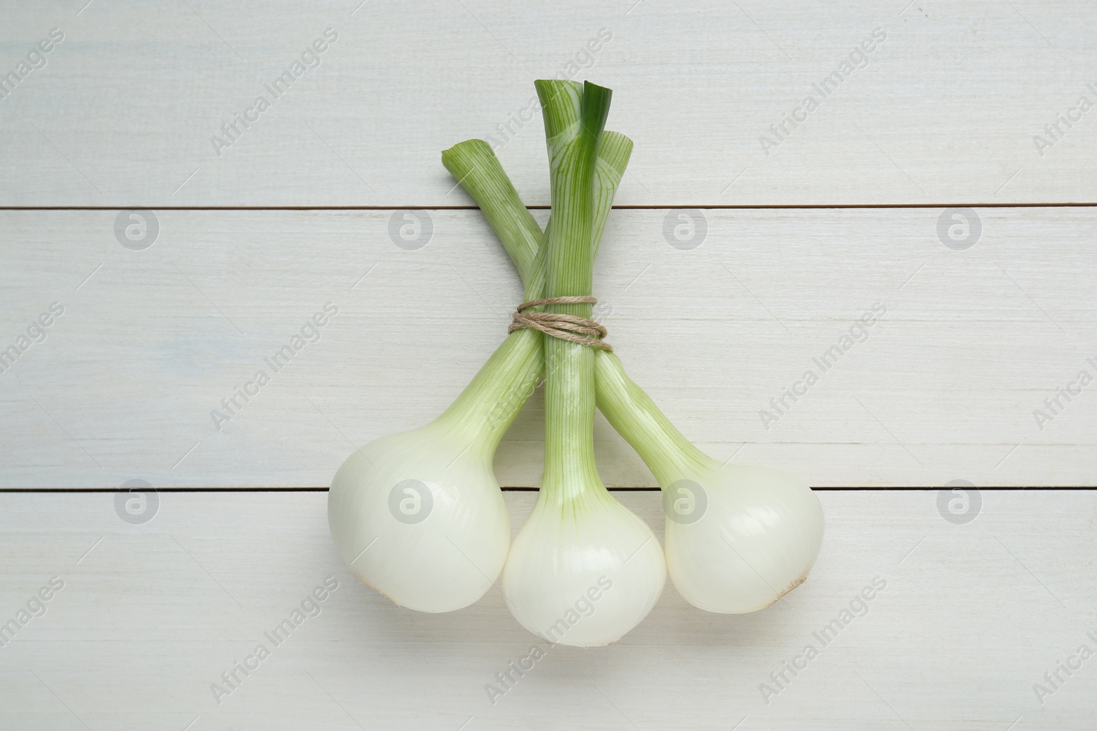 Photo of Bunch of green spring onions on white wooden table, flat lay