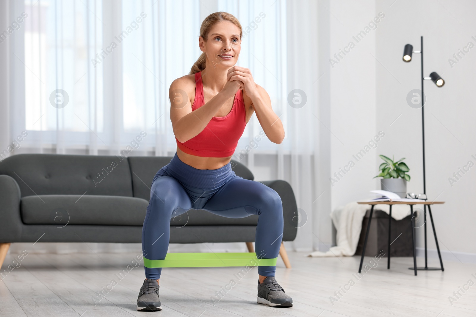 Photo of Fit woman doing squats with fitness elastic band at home
