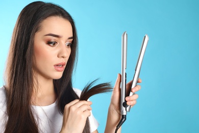 Photo of Emotional woman with hair iron on color background