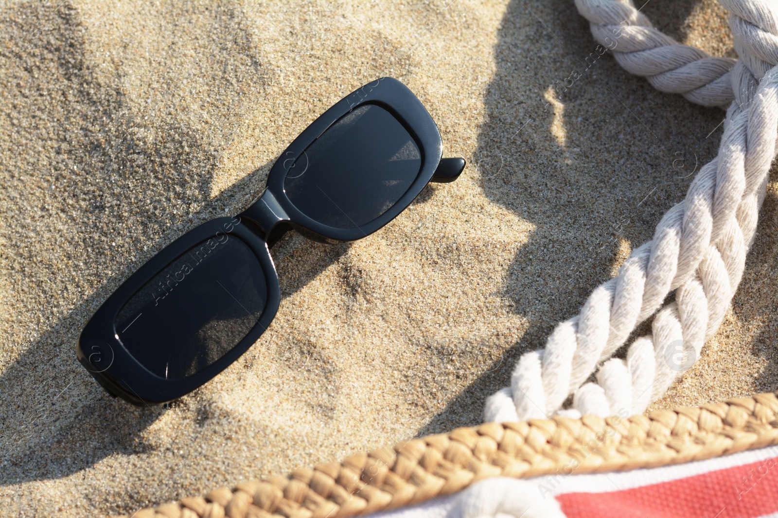 Photo of Stylish sunglasses and beach bag on sand, closeup