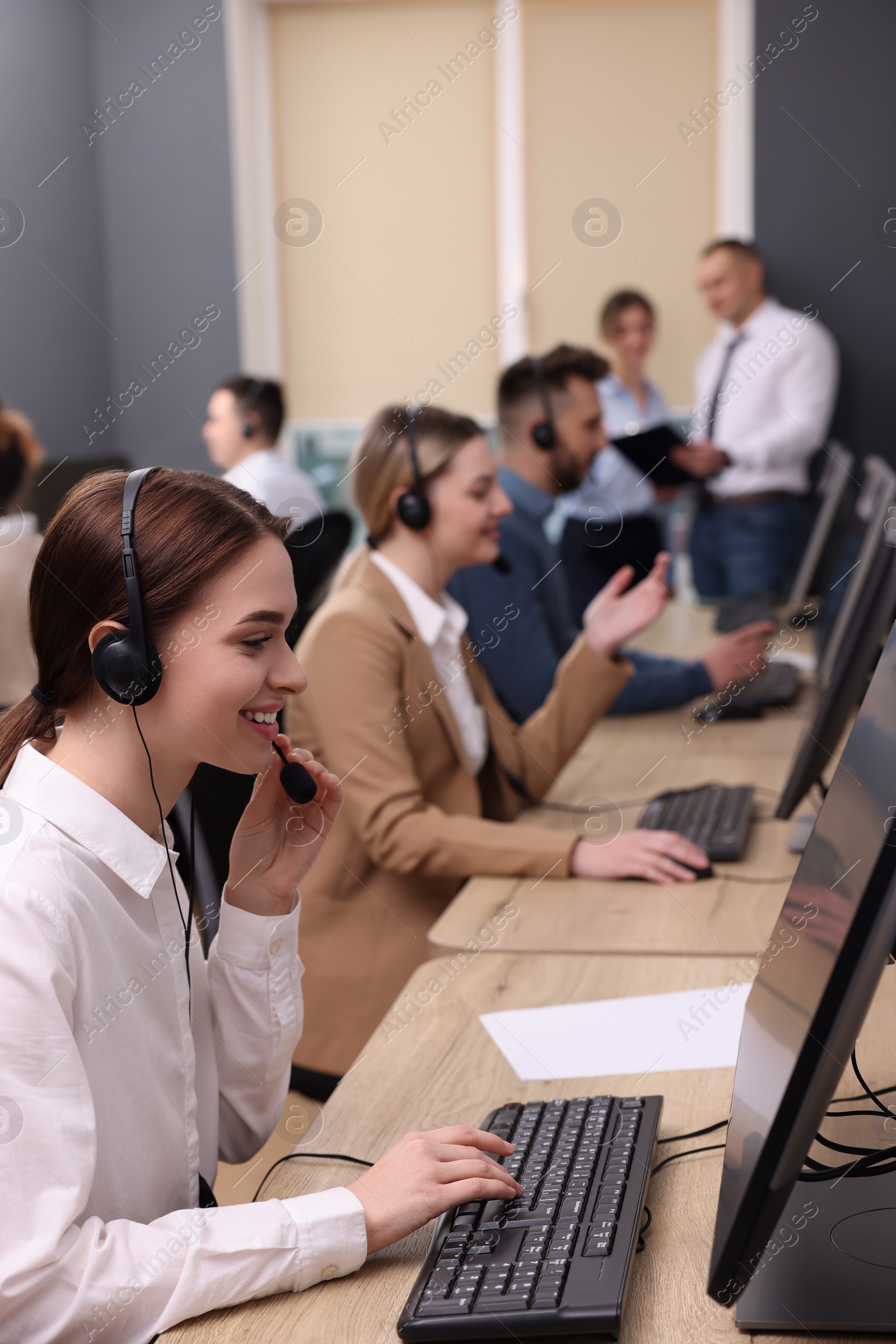 Photo of Call center operators working in modern office, focus on young woman with headset